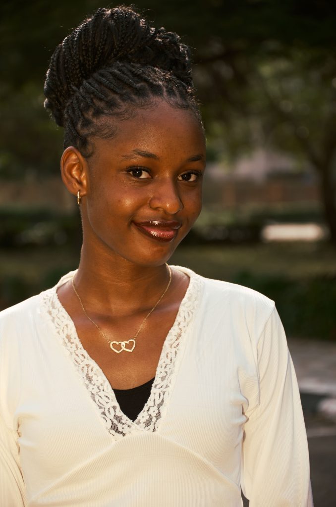 Portrait of a smiling woman with braided hair outdoors, wearing a necklace.