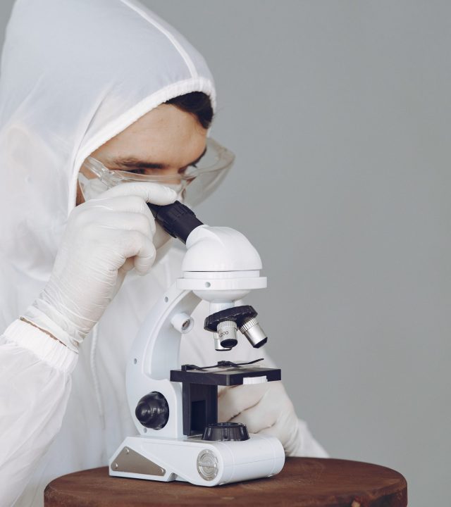 Scientist in protective gear using a microscope, focused on research and analysis.